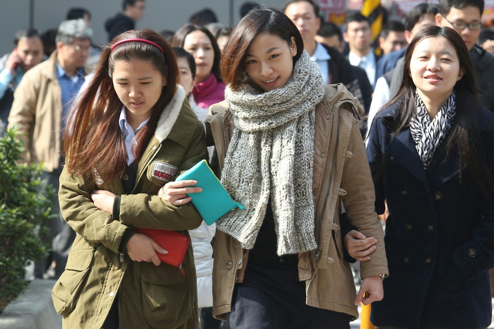 Three women are walking in a crowded street.