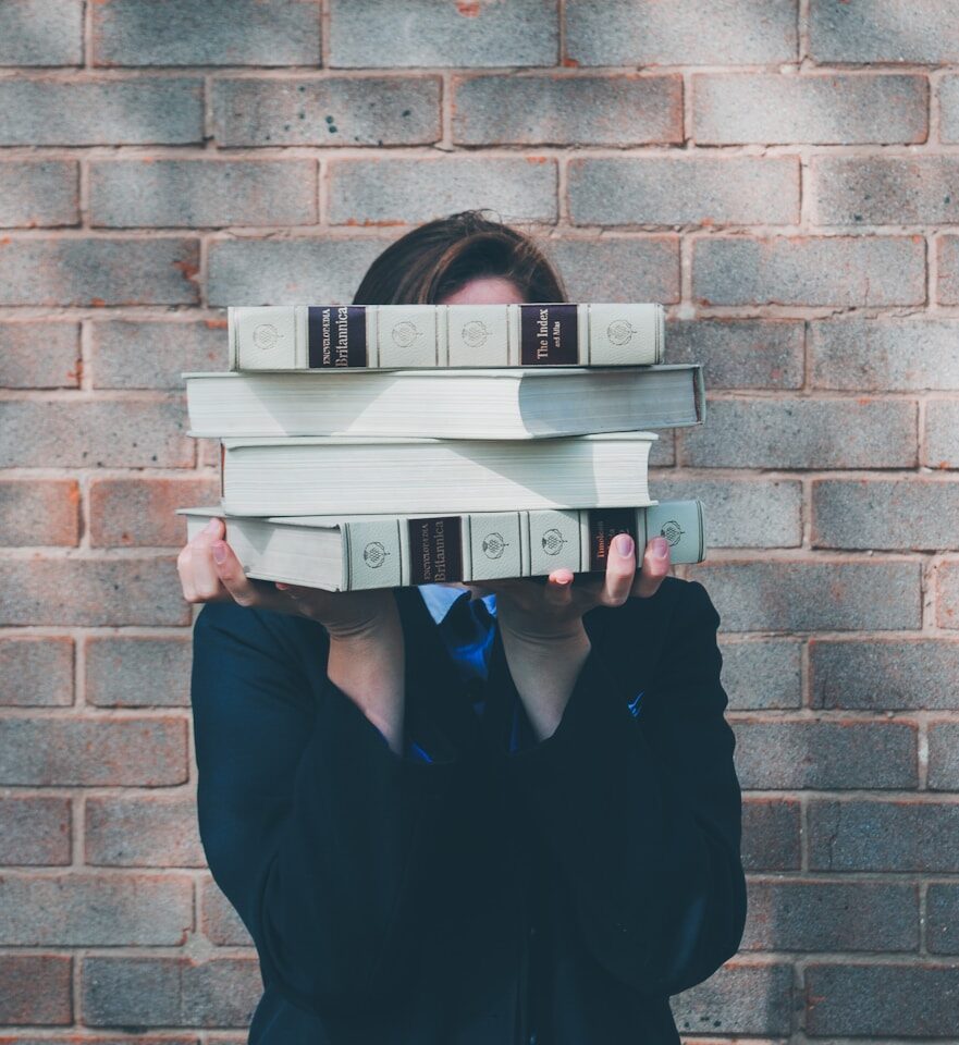 person holding pile of books near face